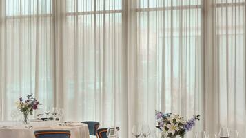 A dining area with round tables set for a meal, featuring chairs with metal frames and cushioned seats.