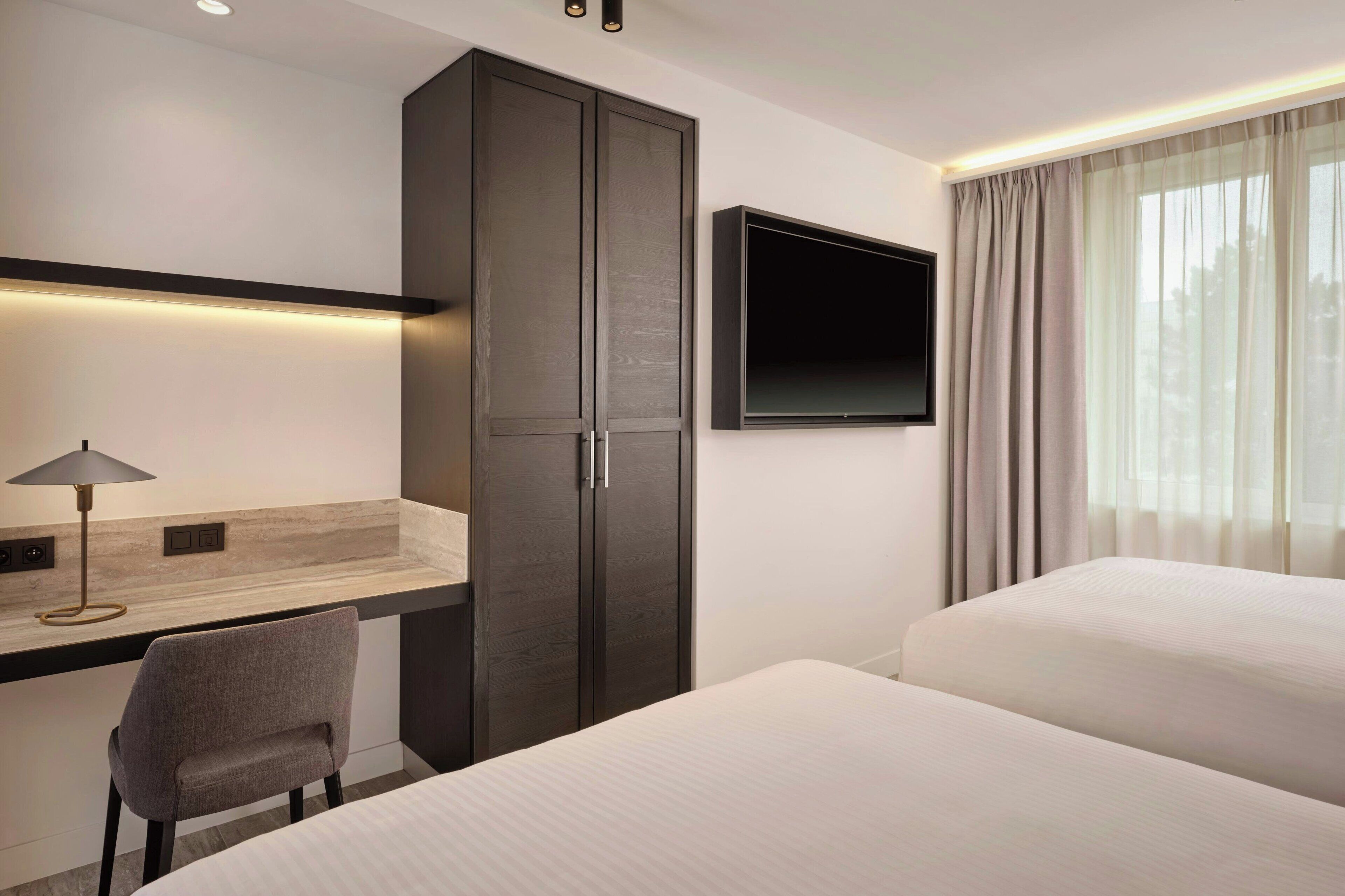 Une chambre d’hôtel équipée d’un bureau, d’une chaise, d’une armoire, d’une télévision et de deux lits.