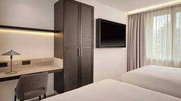 Une chambre d’hôtel équipée d’un bureau, d’une chaise, d’une armoire, d’une télévision et de deux lits.