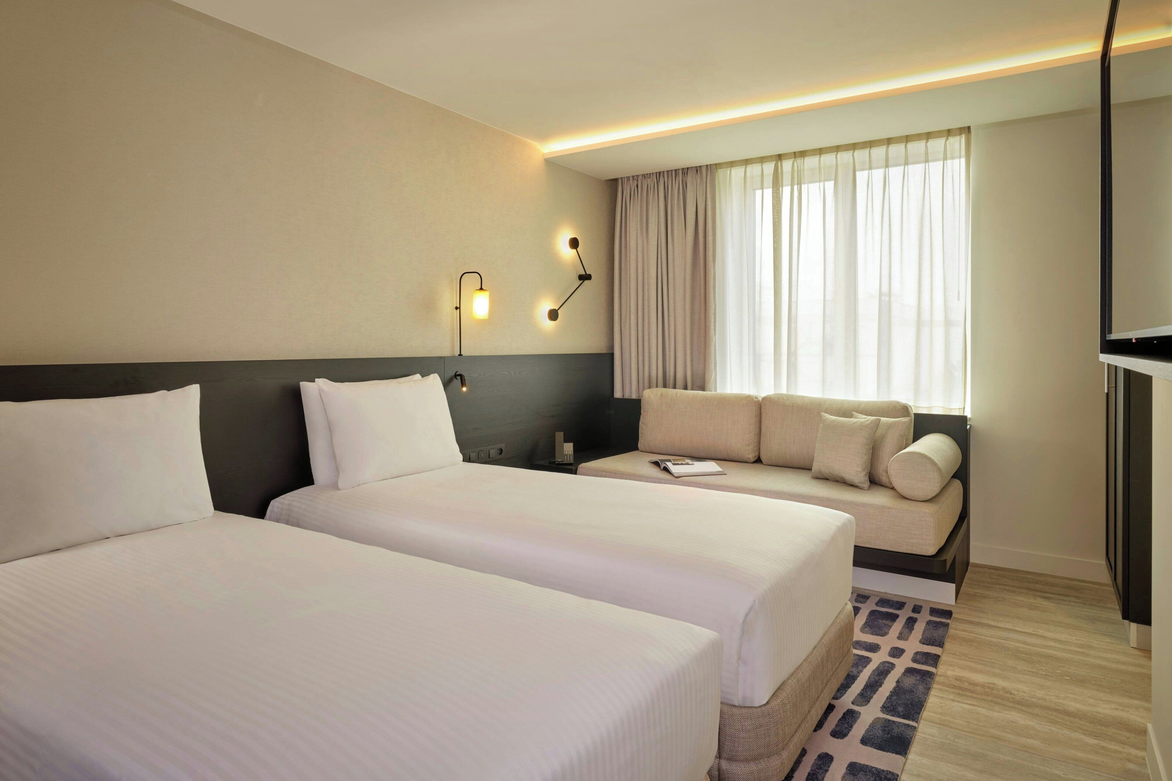 A hotel room with two beds, a sofa, a TV, and a window with curtains.