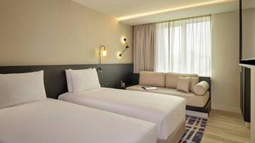 A hotel room with two beds, a sofa, a TV, and a window with curtains.