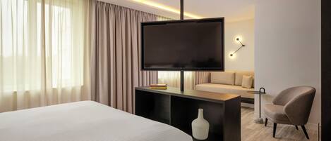 A modern hotel room with a large bed, a flat-screen TV, a sofa, a chair, and a small table.