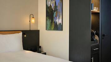 Een hotelkamer met een bed, een bedlamp, een telefoon, een schilderij aan de muur en een kledingkast.