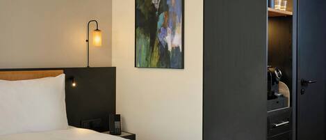 Una habitación de hotel con una cama, una lámpara de noche, un teléfono, un cuadro en la pared y un armario.