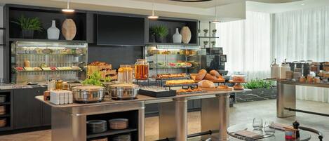 Una barra de desayuno moderna con diversas opciones de alimentos, como frutas, pasteles y bebidas.