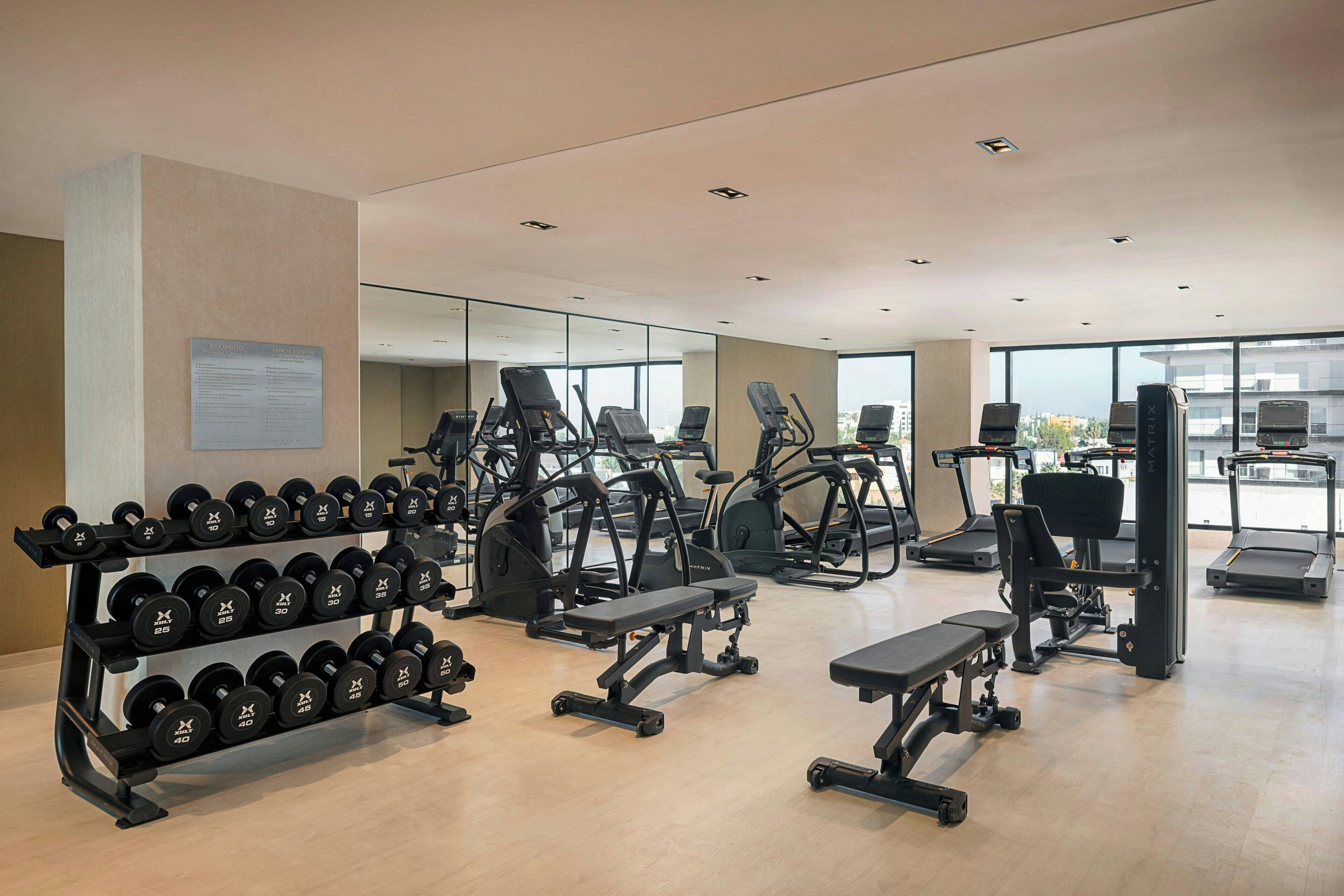 Une salle de sport moderne équipée de divers appareils d’exercice, notamment des tapis de course, des vélos elliptiques et des poids libres.