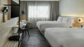 A hotel room with two beds, a desk, a chair, a TV, and a window with curtains.
