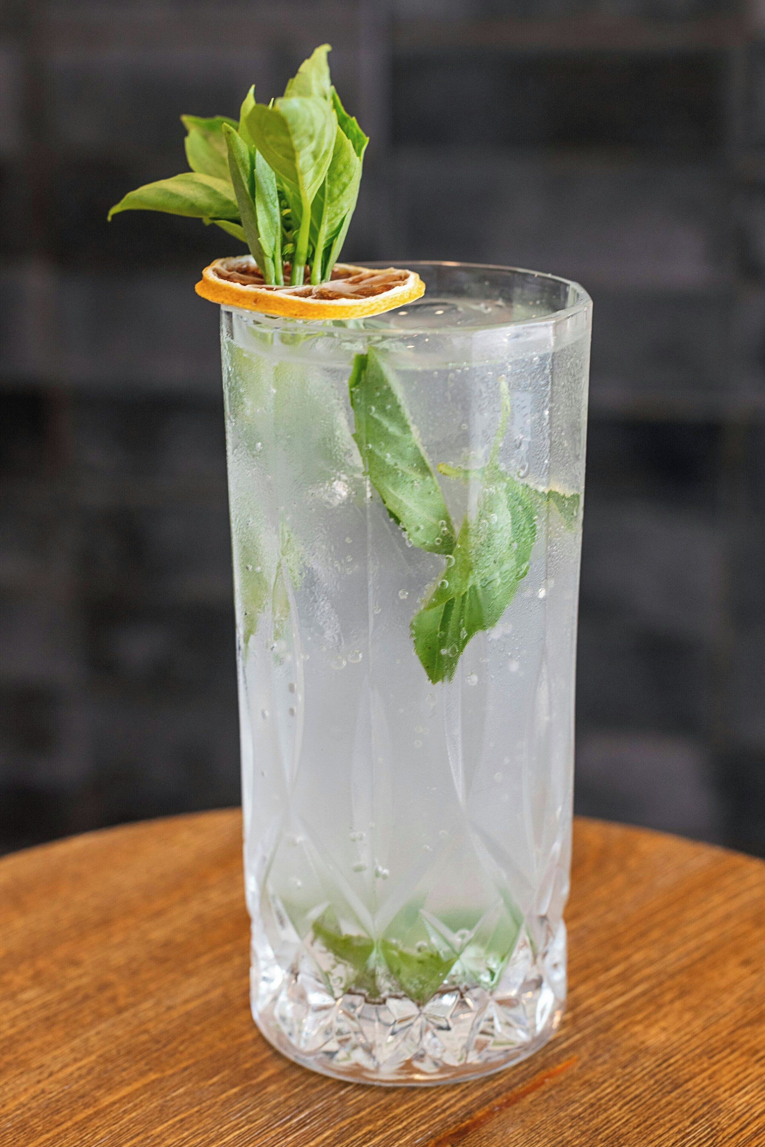 Un grand verre contenant un liquide transparent, des feuilles de menthe et une tranche d’orange en guise de décoration, posé sur une surface en bois.