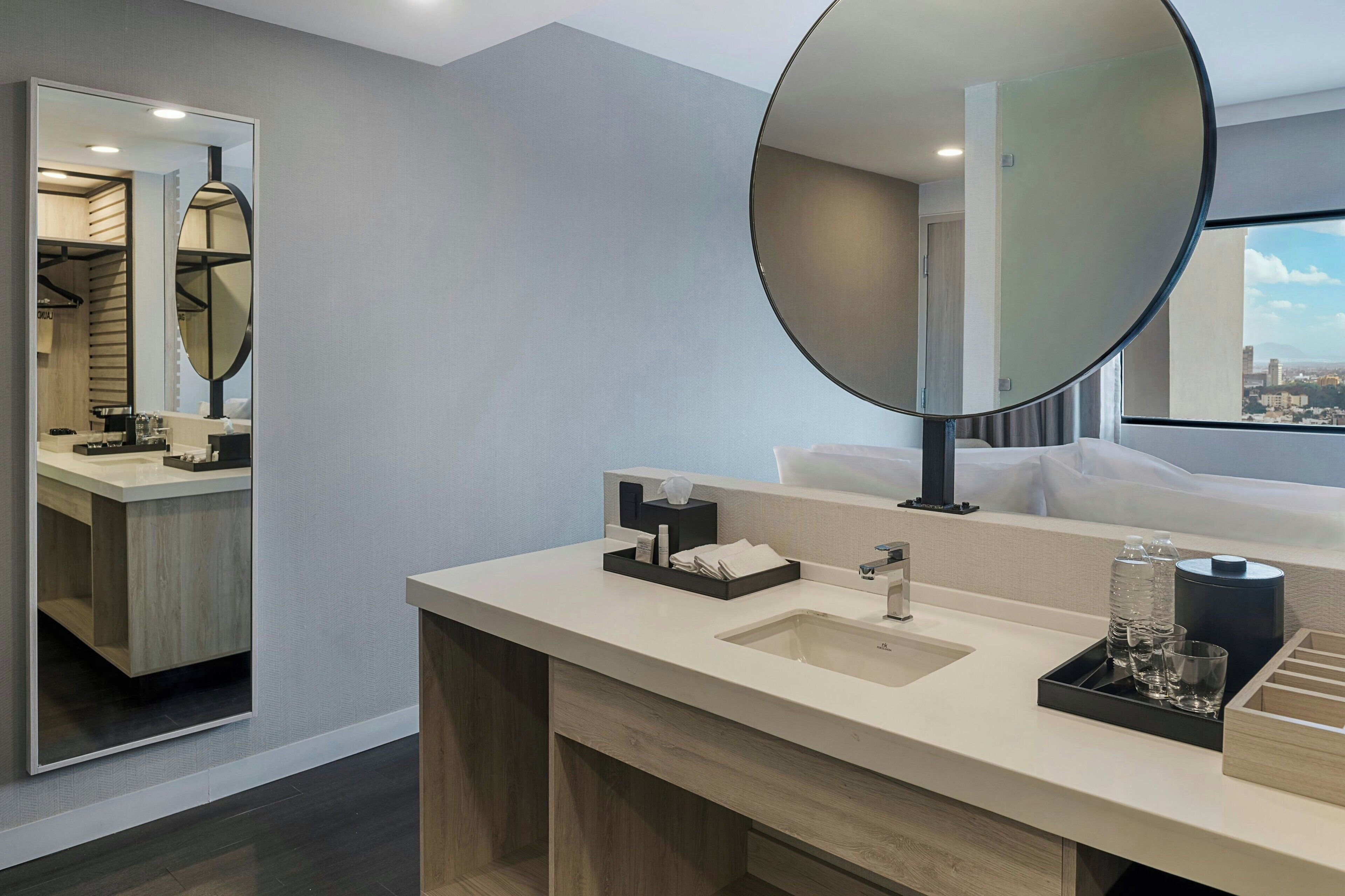 A modern hotel bathroom with a large mirror, a sink, and a vanity area.