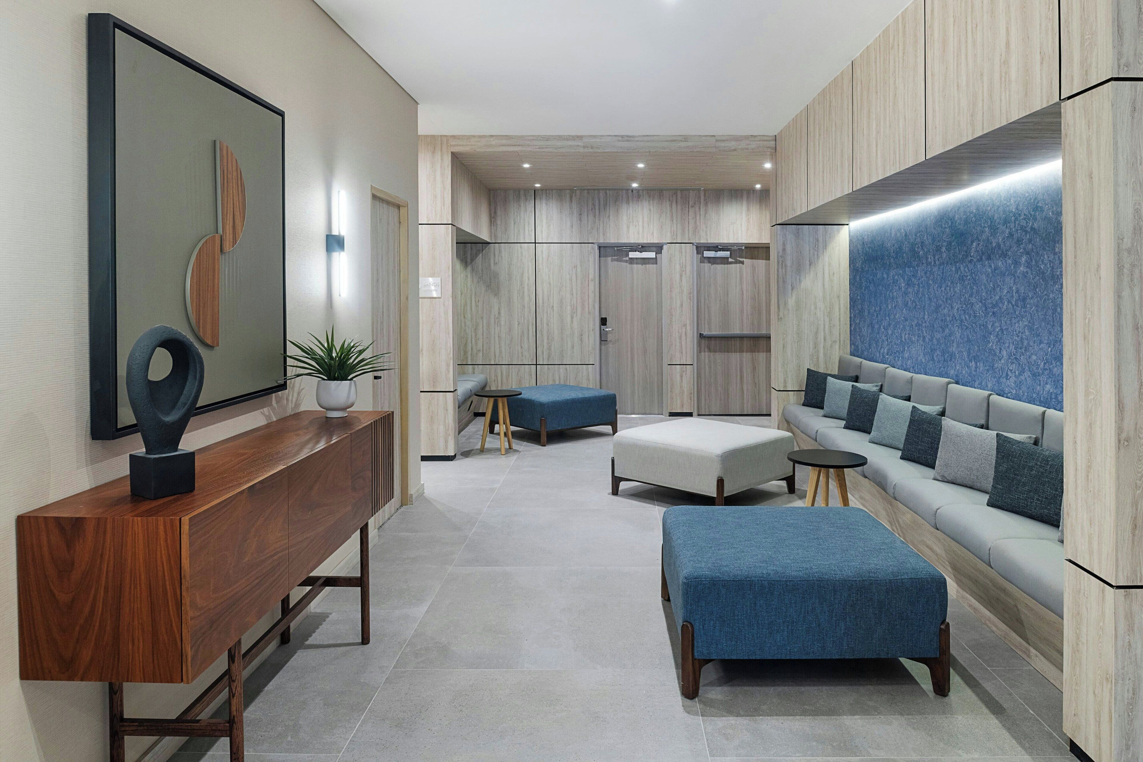 Un interior moderno con una consola de madera, otomanas azules, un sofá gris y un televisor montado en la pared.