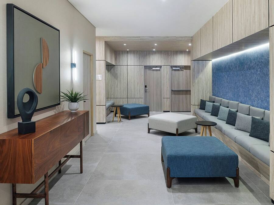 Een modern interieur met een houten consoles, blauwe poefs, een grijze bank en een wandgemonteerde televisie.