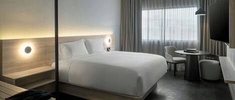 Ein modernes Hotelzimmer mit einem großen Bett, Nachttischen, einem Schreibtisch mit Stuhl, einem runden Tisch und einem Fernseher.