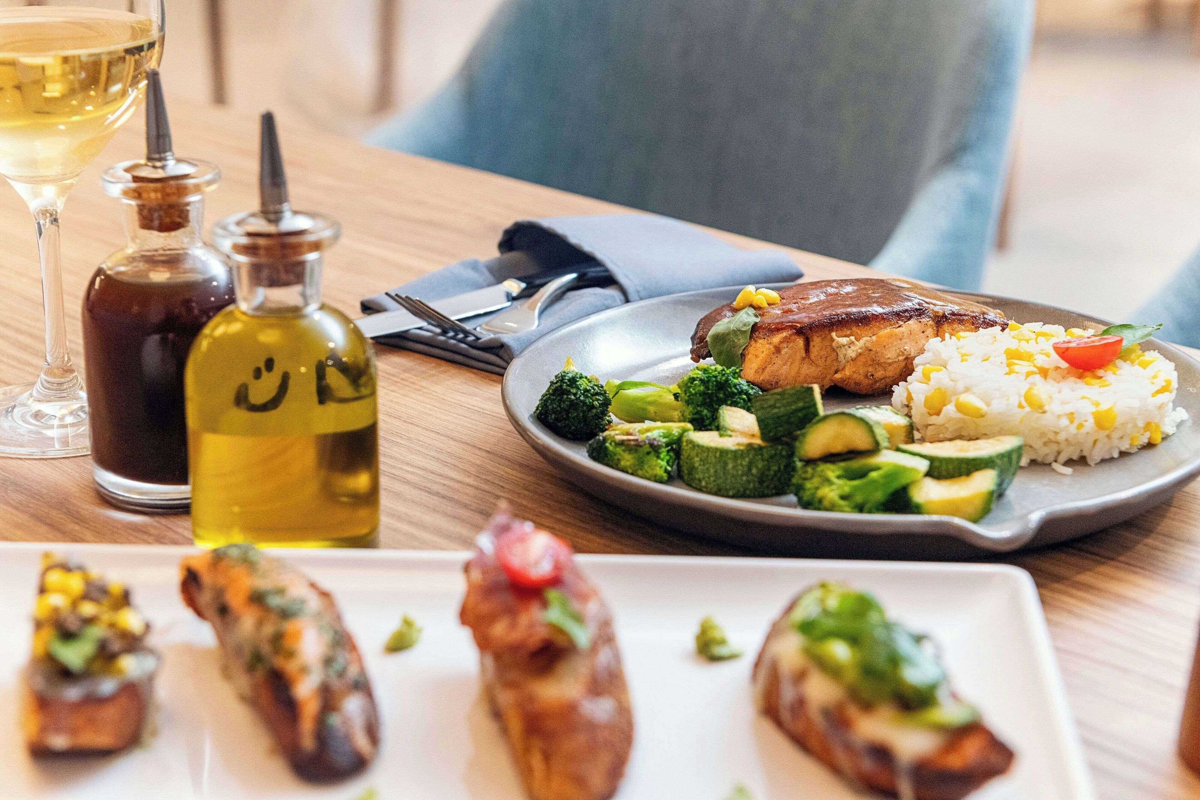 A dining table with a plate of food, a bottle of oil, and a glass of wine.