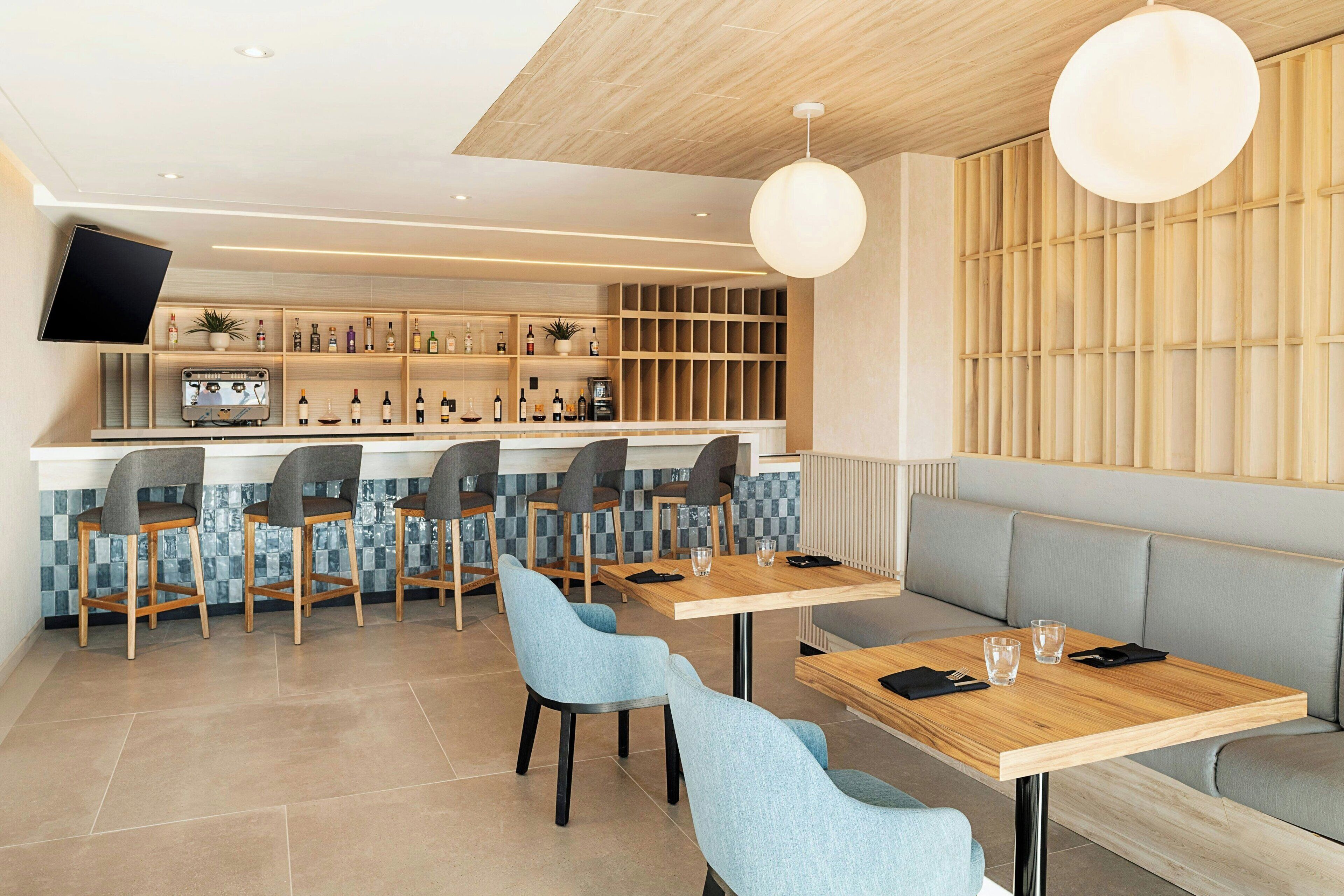 Un restaurante moderno con zona de bar, mesas y sillas, y un televisor montado en la pared.