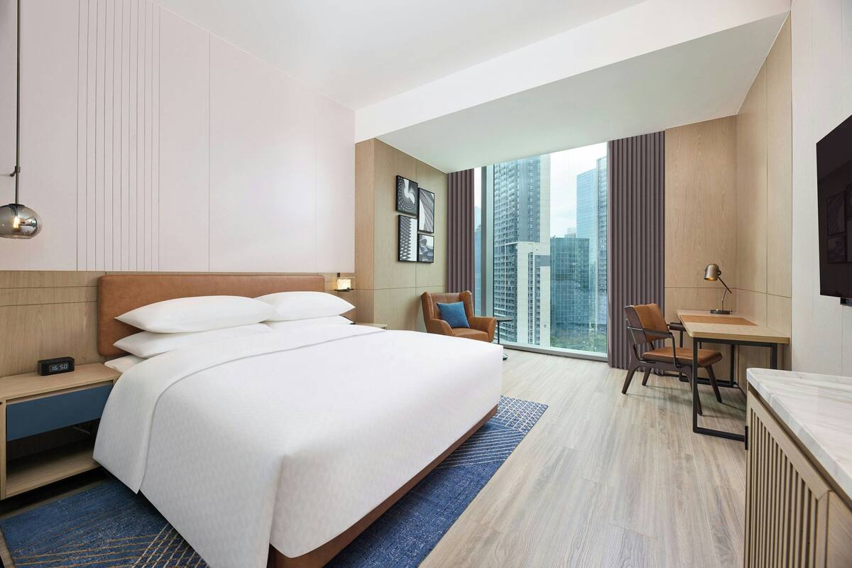 A modern hotel room with a large bed, a desk, and a view of the city.