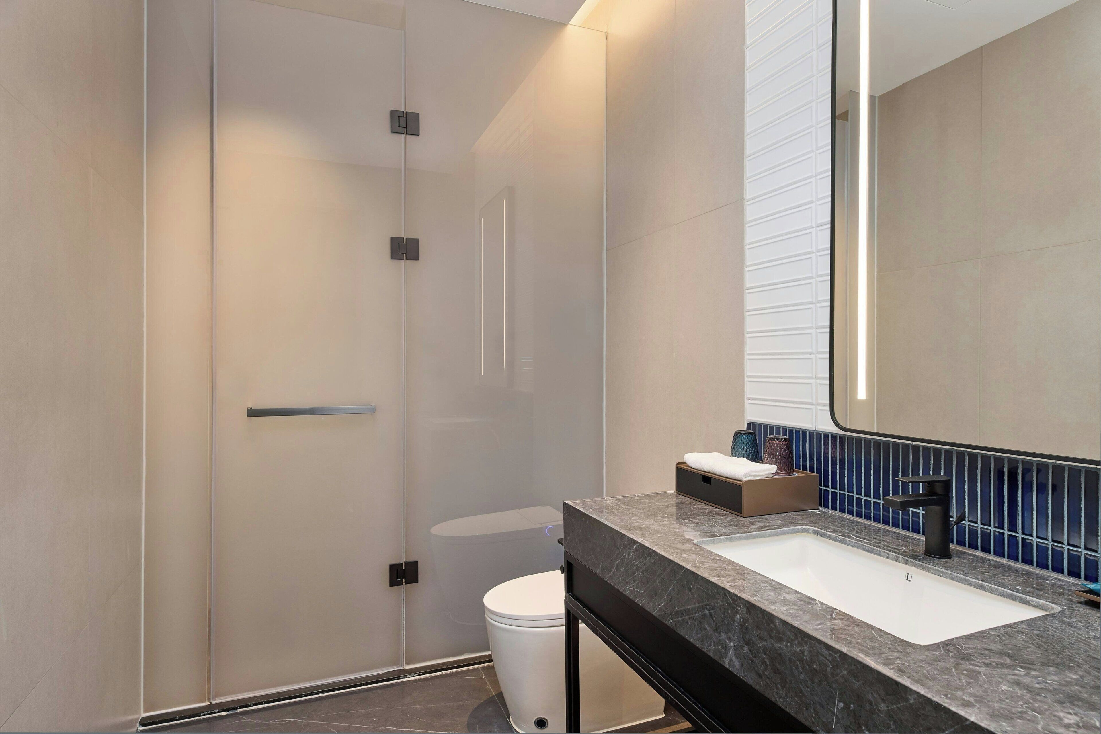 A modern bathroom with a glass shower enclosure, a white sink with a black faucet, and a mirror with a blue-tiled backsplash.