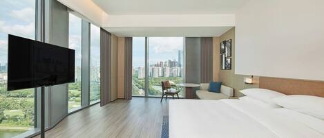 Habitación de hotel con una cama grande, televisión, escritorio y vista a un paisaje urbano.