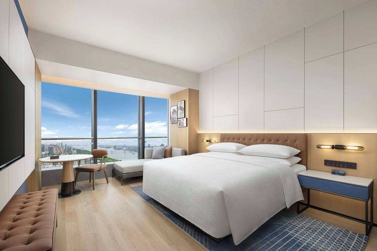 Une chambre d’hôtel moderne, dotée d’un grand lit, d’un bureau, d’une chaise et offrant une vue sur la ville.