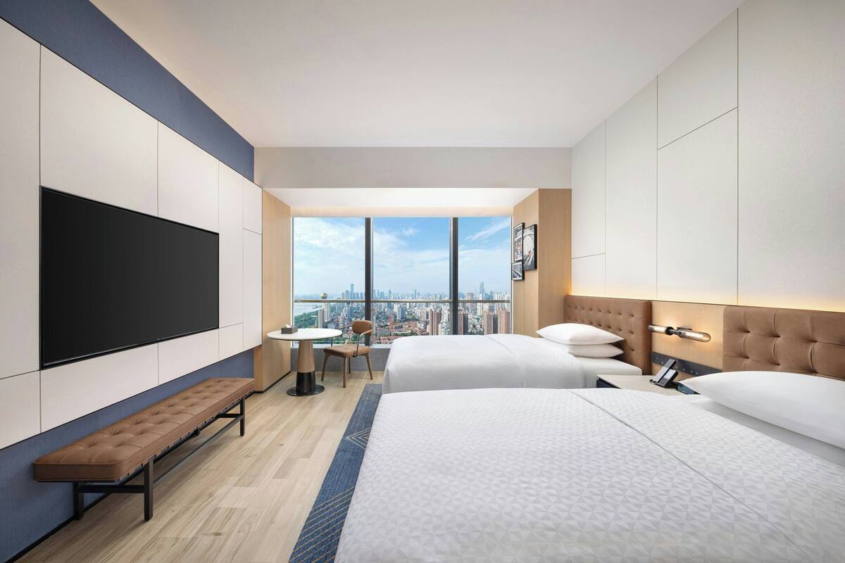 Une chambre d’hôtel avec deux lits, un banc, une télévision, un bureau et une vue sur la ville.