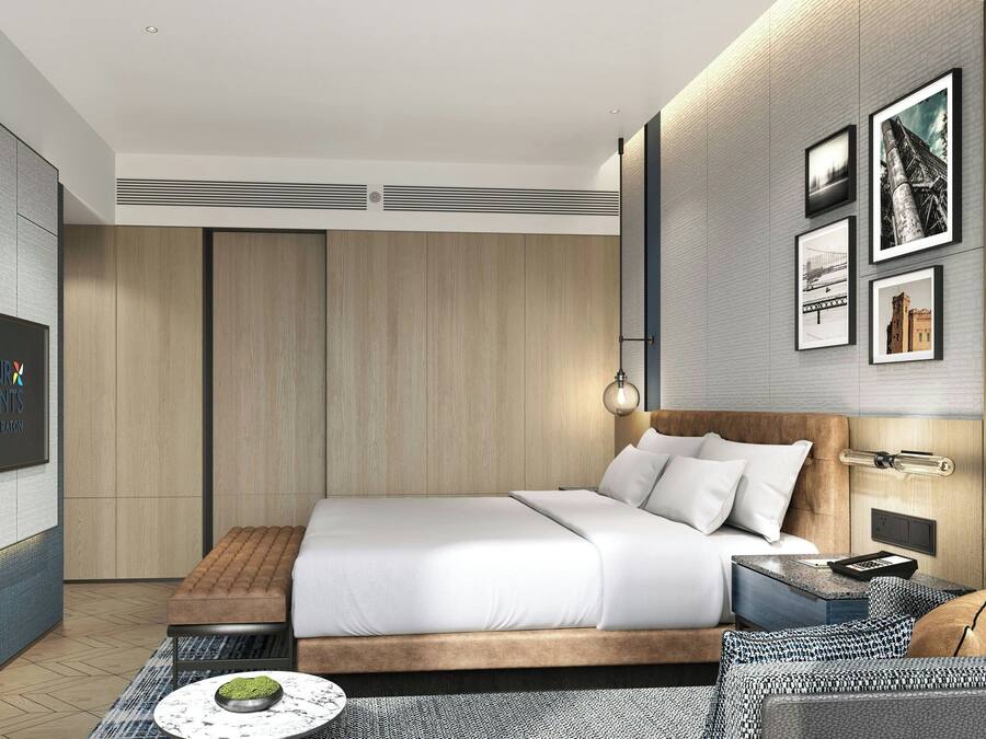 A modern hotel room with a large bed, a flat-screen TV, a wooden wardrobe, and framed pictures on the wall.