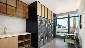 A modern laundry room with a row of washing machines, a sink, and a dining area with a table and chairs. - Four Points By Sheraton Wuhan Hankou (Wuhan)