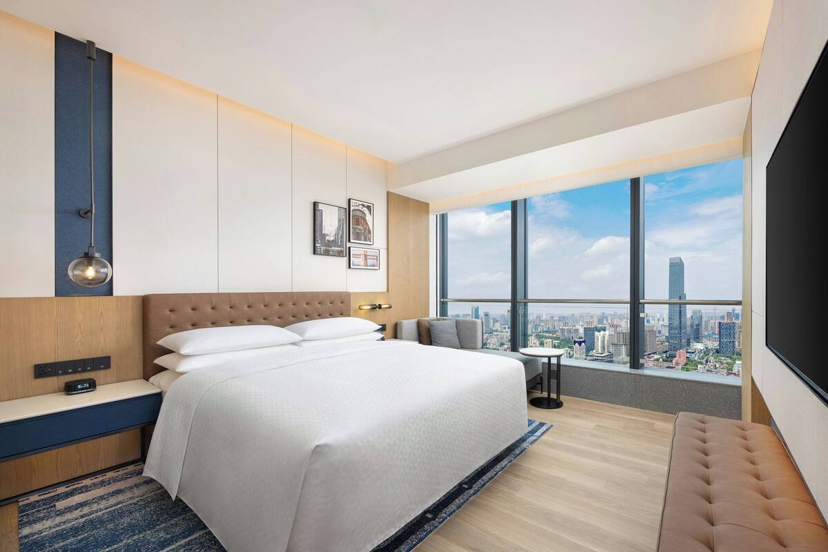 Une chambre d’hôtel moderne dotée d’un grand lit, d’un coin salon, d’une télévision et offrant une vue sur la ville.