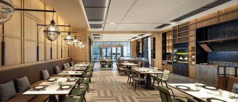 A modern restaurant interior with long communal tables, green chairs, and pendant lighting.