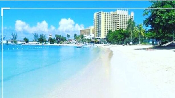A beachfront hotel with a large building, a sandy beach, and clear blue water.