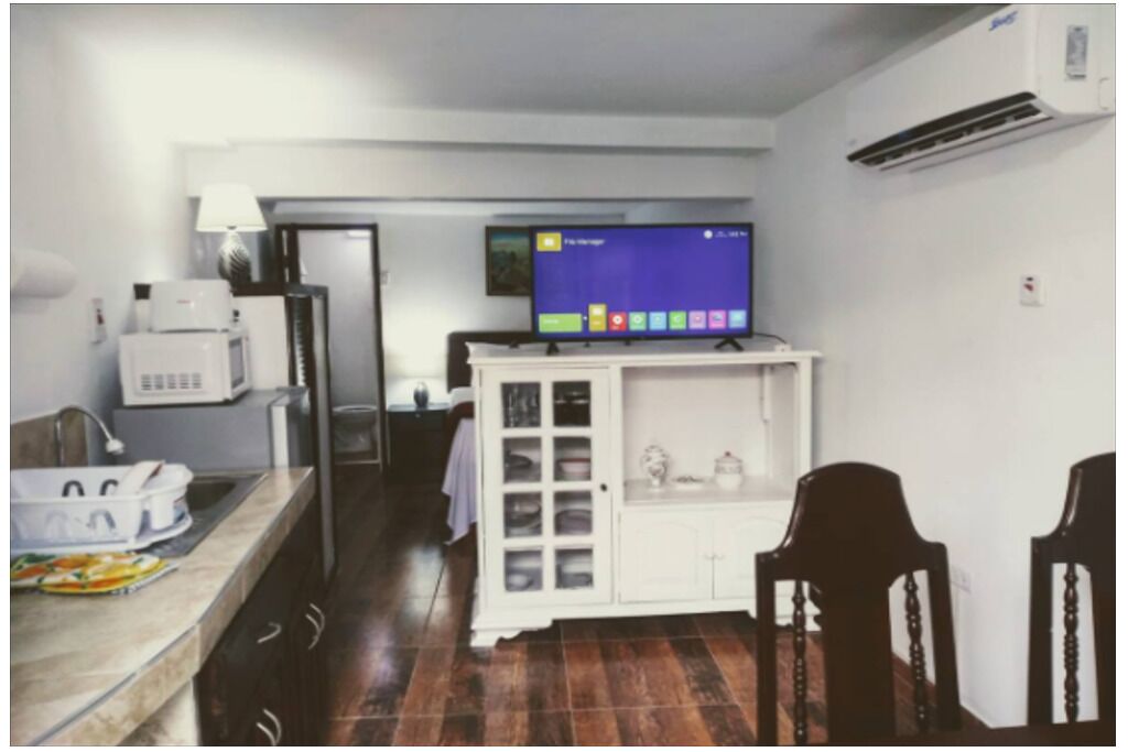 A compact kitchen with a microwave, a small refrigerator, a cabinet with glass doors, and a television on a stand.