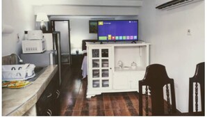 A compact kitchen with a microwave, a small refrigerator, a cabinet with glass doors, and a television on a stand.