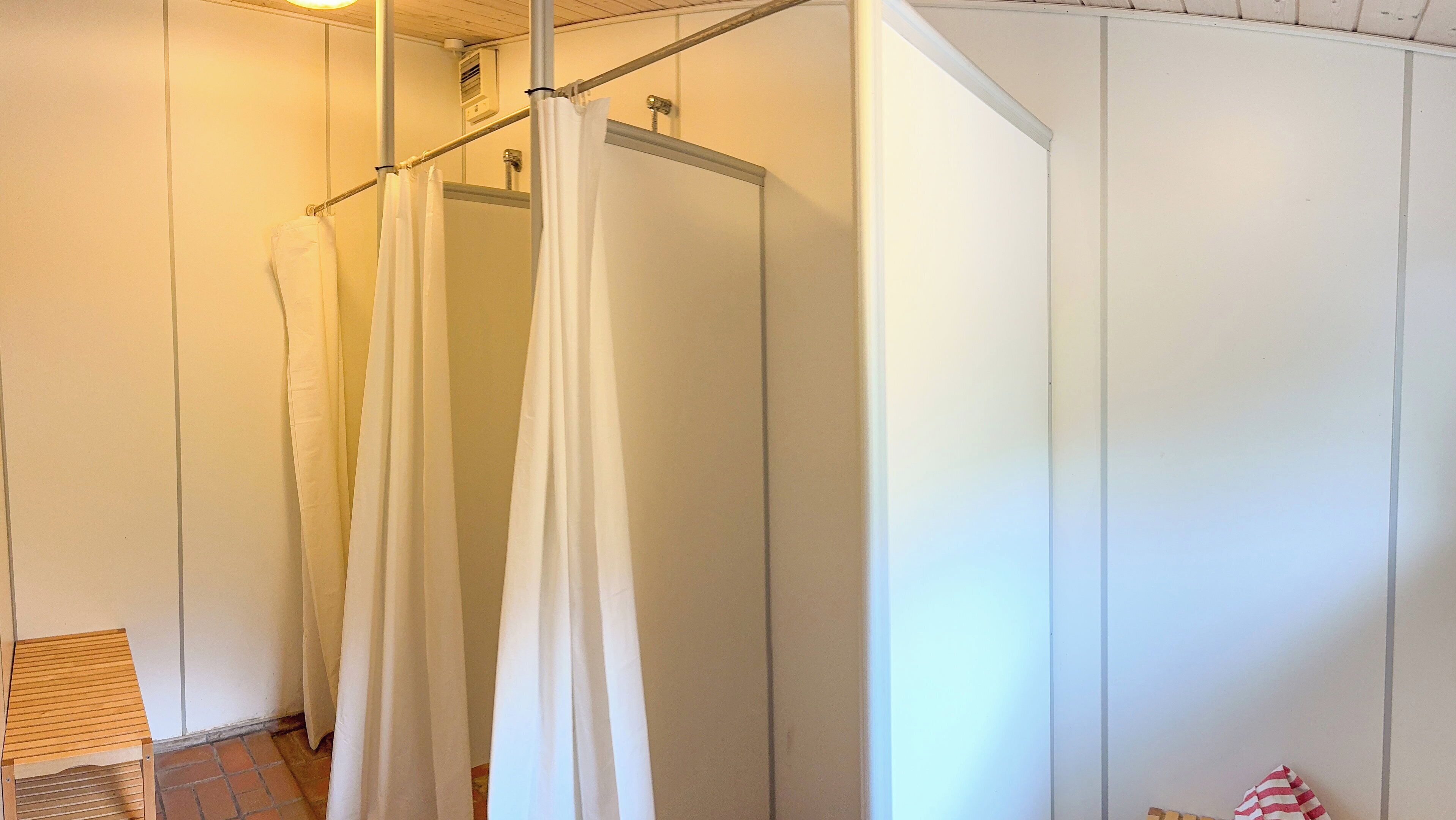 Eine Dusche mit einer Metallstange und weißen Vorhängen, einem hölzernen Hocker und einem Fliesenboden.
