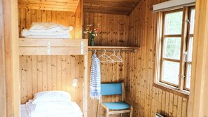 A wooden cabin interior with a bunk bed, a small seating area, a window, and a hanging clothes rack.