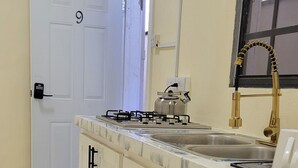 A kitchen with a white door marked with the number 9, a gas stove, a sink with a gold faucet, and black and white patterned mats on the floor. - Beautiful apartment with AC in Saint George's (Saint George's)
