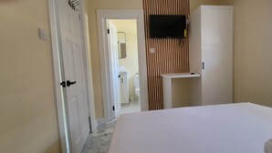 A hotel room with a bed, a television mounted on the wall, a small table, and a window with blinds. - Beautiful apartment with AC in Saint George's (Saint George's)