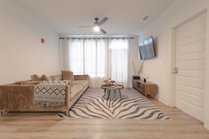A living room with a sofa, a coffee table, a ceiling fan, and a TV mounted on the wall.