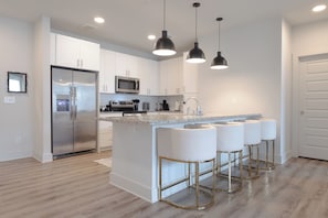 A modern kitchen with white cabinets, stainless steel appliances, a granite countertop, and gold bar stools.