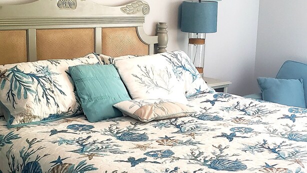 Un dormitorio con cama, mesita de noche, lámpara y un marco en la pared.