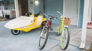 Un porche cubierto con un bote amarillo y blanco, una bicicleta roja y otra bicicleta verde estacionadas.
