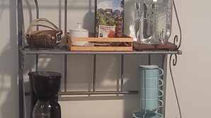 Una estantería metálica con una encimera de madera, una cafetera, un horno tostador y un tarro de cristal.