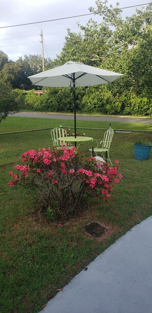 A patio with a table and chairs, a green umbrella, and pink flowers.