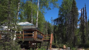 Une cabane en bois dotée d’une terrasse, entourée d’arbres et bordée d’un chemin de gravier.