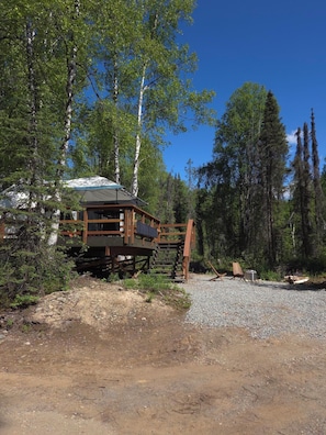Une cabane en bois dotée d’une terrasse, entourée d’arbres et bordée d’un chemin de gravier.