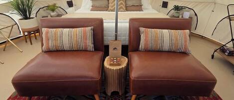 A tent with a bed, two leather sofas, a patterned rug, and potted plants.