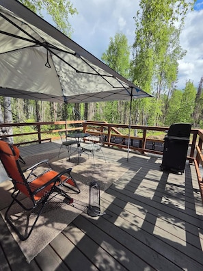 Une terrasse dotée d’un espace salon couvert, d’un barbecue et offrant une vue sur une forêt.