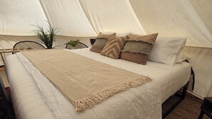 Une pièce aménagée comme une tente, avec un lit, des oreillers, une couverture et une petite plante.