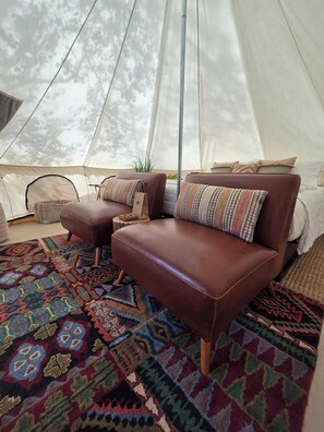 Une tente avec un canapé et un pouf en cuir marron, un tapis à motifs et une petite table d’appoint.