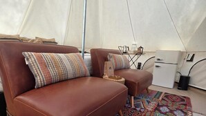 Et teltindretning med en brun lædersofa, en matchende skammel, et mønstret tæppe og et hvidt køleskab.