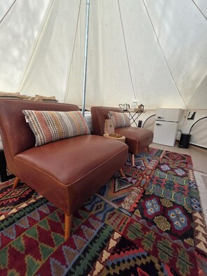 A tent interior with a brown leather sofa, a matching ottoman, a patterned rug, and a white refrigerator. - Glamping in the trees (Talkeetna)