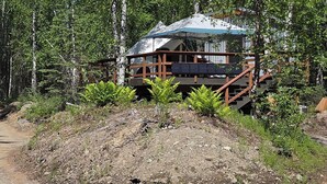 Une cabane dotée d’une terrasse en bois, entourée d’arbres et accessible par un sentier de terre.