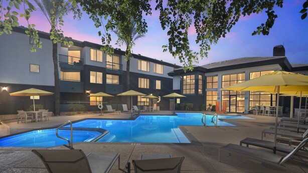 A hotel pool area with lounge chairs and umbrellas, surrounded by buildings with large windows and balconies. - Central Relaxing 1br Phoenix Retreat Near Airport 1 Bedroom Apts (Phoenix)